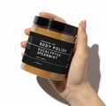 Hand holding a jar of body polish labeled 'Eucalyptus Spearmint' on a white background