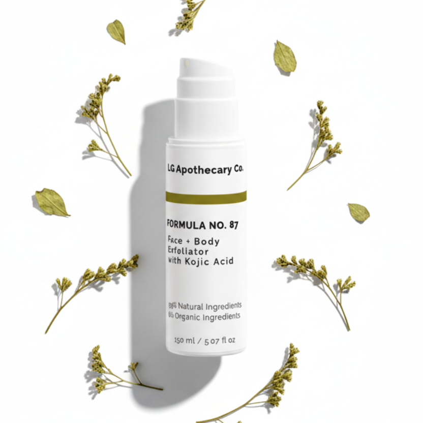 White pump bottle of Formula No. 87 Face & Body Exfoliator with Kojic Acid centered on a white background, surrounded by dried yellow botanical sprigs and leaves with soft shadows.